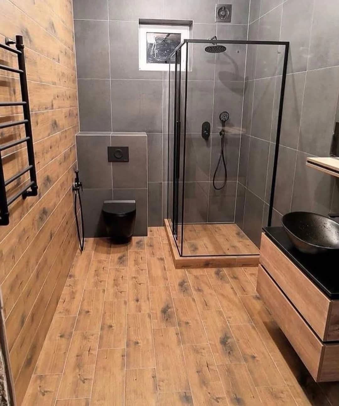 Ahşap görünümlü yüzeyler, gri duvarlar ve siyah armatürlerin bulunduğu banyo